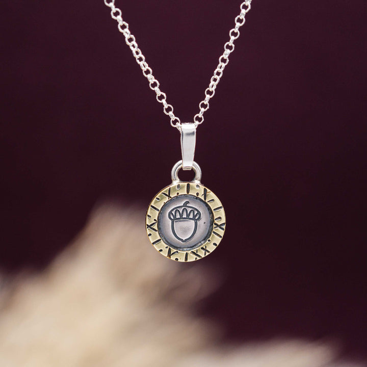 Eine kurze Silberkette aus Sterling Silber 925 mit einem kleinen gravierten Eichel Anhänger, eingerahmt von einem goldenem Rahmen.