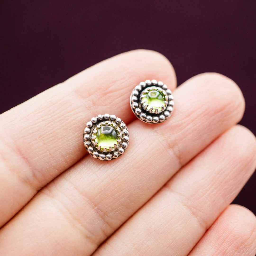 Kleine Peridot Ohrstecker aus Silber 925 mit hellgrünem Stein und detailreicher Kugelverzierung auf einer Hand