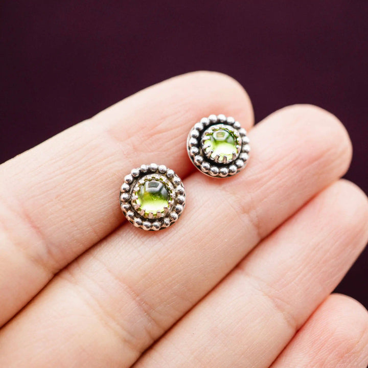 Kleine Peridot Ohrstecker aus Silber 925 mit hellgrünem Stein und detailreicher Kugelverzierung auf einer Hand