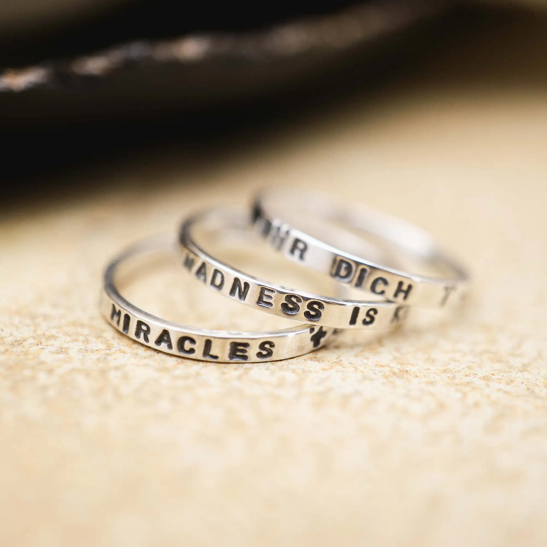 Schmaler Ring mit personalisierter Gravur aus Sterling Silber 925. In den dünnen Silberring sind Buchstaben und Texturen gehämmert nach individuellem Wunsch der Kundin. Auf einem Ring ist der Text “Open to Miracles” zu lesen, auf einem anderen ist der Spruch “A little bit of Madness is Key” eingraviert. Den dritten silbernen Ring zieren die Worte “Mädel, machs für dich”.