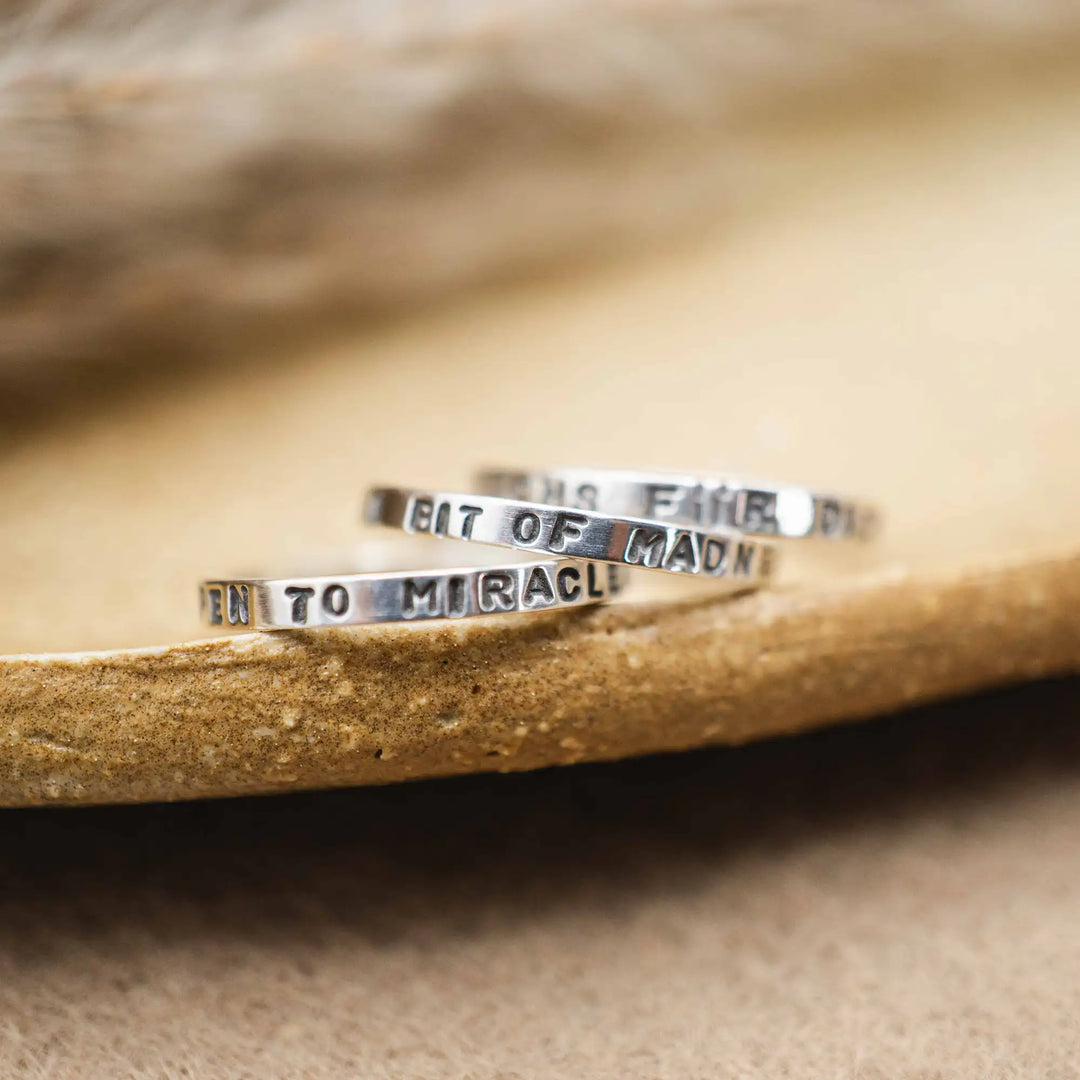 Schmaler Ring mit personalisierter Gravur aus Sterling Silber 925. In den dünnen Silberring sind Buchstaben und Texturen gehämmert nach individuellem Wunsch der Kundin. Auf einem Ring ist der Text “Open to Miracles” zu lesen, auf einem anderen ist der Spruch “A little bit of Madness is Key” eingraviert. Den dritten silbernen Ring zieren die Worte “Mädel, machs für dich”.