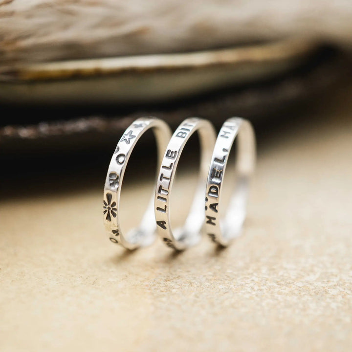 Schmaler Ring mit personalisierter Gravur aus Sterling Silber 925. In den dünnen Silberring sind Buchstaben und Texturen gehämmert nach individuellem Wunsch der Kundin. Auf einem Ring ist der Text “Open to Miracles” zu lesen, auf einem anderen ist der Spruch “A little bit of Madness is Key” eingraviert. Den dritten silbernen Ring zieren die Worte “Mädel, machs für dich”.