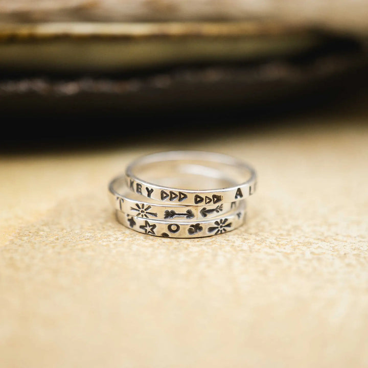 Schmaler Ring mit personalisierter Gravur aus Sterling Silber 925. In den dünnen Silberring sind Buchstaben und Texturen gehämmert nach individuellem Wunsch der Kundin. Auf einem Ring ist der Text “Open to Miracles” zu lesen, auf einem anderen ist der Spruch “A little bit of Madness is Key” eingraviert. Den dritten silbernen Ring zieren die Worte “Mädel, machs für dich”.