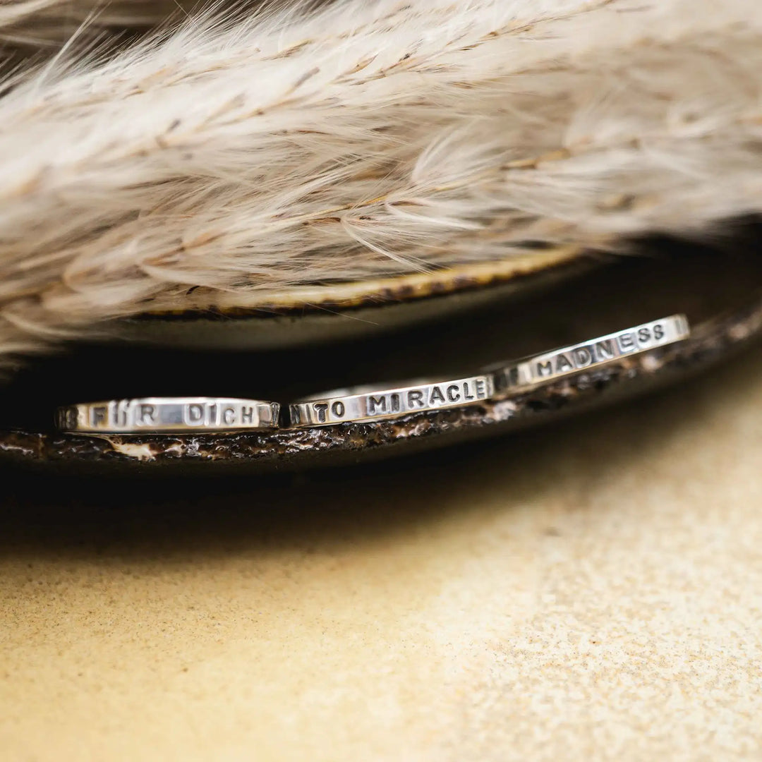 Schmaler Ring mit personalisierter Gravur aus Sterling Silber 925. In den dünnen Silberring sind Buchstaben und Texturen gehämmert nach individuellem Wunsch der Kundin. Auf einem Ring ist der Text “Open to Miracles” zu lesen, auf einem anderen ist der Spruch “A little bit of Madness is Key” eingraviert. Den dritten silbernen Ring zieren die Worte “Mädel, machs für dich”.