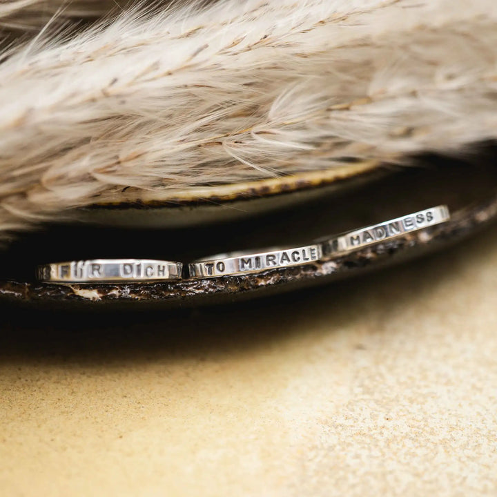 Schmaler Ring mit personalisierter Gravur aus Sterling Silber 925. In den dünnen Silberring sind Buchstaben und Texturen gehämmert nach individuellem Wunsch der Kundin. Auf einem Ring ist der Text “Open to Miracles” zu lesen, auf einem anderen ist der Spruch “A little bit of Madness is Key” eingraviert. Den dritten silbernen Ring zieren die Worte “Mädel, machs für dich”.