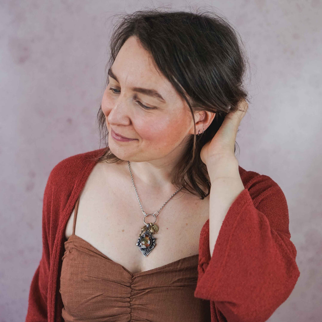 Statement Kette groß aus Silber 925. In den Anhänger eingefasst ist ein tropfenförmiger Lodolith, auch Gartenquarz genannt. Der Stein sieht aus wie eingeschlossenes grünes, gelbes und orangefarbenes Moos und ist umrandet von Pilzen, Blättern und Knospen. Ein echtes, handgefertigtes Statement Piece an Naturschmuck.
An dem Anhänger hängen außerdem 3 kleine Charms aus Messing: Ein Marienkäfer, ein Pilz und ein Blatt.