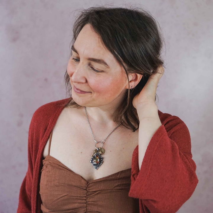 Statement Kette groß aus Silber 925. In den Anhänger eingefasst ist ein tropfenförmiger Lodolith, auch Gartenquarz genannt. Der Stein sieht aus wie eingeschlossenes grünes, gelbes und orangefarbenes Moos und ist umrandet von Pilzen, Blättern und Knospen. Ein echtes, handgefertigtes Statement Piece an Naturschmuck.
An dem Anhänger hängen außerdem 3 kleine Charms aus Messing: Ein Marienkäfer, ein Pilz und ein Blatt.