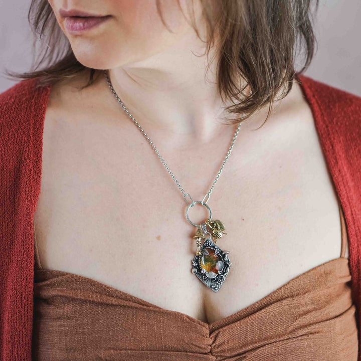 Statement Kette groß aus Silber 925. In den Anhänger eingefasst ist ein tropfenförmiger Lodolith, auch Gartenquarz genannt. Der Stein sieht aus wie eingeschlossenes grünes, gelbes und orangefarbenes Moos und ist umrandet von Pilzen, Blättern und Knospen. Ein echtes, handgefertigtes Statement Piece an Naturschmuck.
An dem Anhänger hängen außerdem 3 kleine Charms aus Messing: Ein Marienkäfer, ein Pilz und ein Blatt.