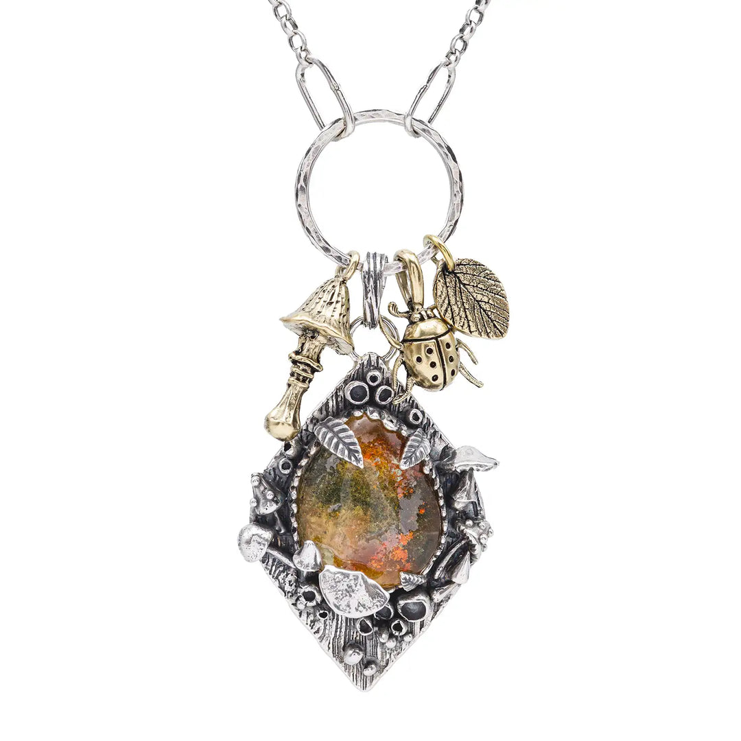 Statement Kette groß aus Silber 925. In den Anhänger eingefasst ist ein tropfenförmiger Lodolith, auch Gartenquarz genannt. Der Stein sieht aus wie eingeschlossenes grünes, gelbes und orangefarbenes Moos und ist umrandet von Pilzen, Blättern und Knospen. Ein echtes, handgefertigtes Statement Piece an Naturschmuck.
An dem Anhänger hängen außerdem 3 kleine Charms aus Messing: Ein Marienkäfer, ein Pilz und ein Blatt.