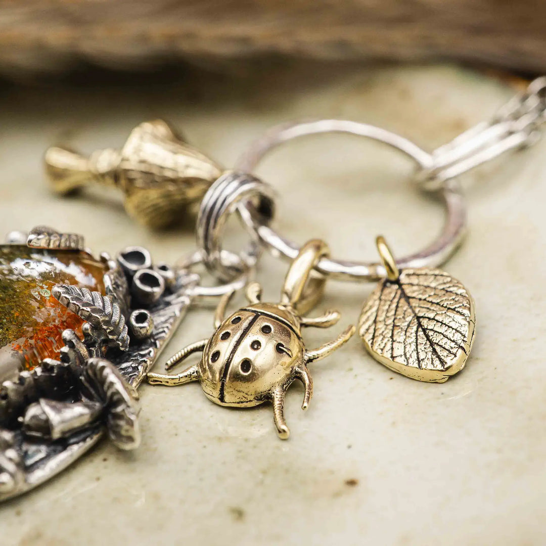 Statement Kette groß aus Silber 925. In den Anhänger eingefasst ist ein tropfenförmiger Lodolith, auch Gartenquarz genannt. Der Stein sieht aus wie eingeschlossenes grünes, gelbes und orangefarbenes Moos und ist umrandet von Pilzen, Blättern und Knospen. Ein echtes, handgefertigtes Statement Piece an Naturschmuck.
An dem Anhänger hängen außerdem 3 kleine Charms aus Messing: Ein Marienkäfer, ein Pilz und ein Blatt.