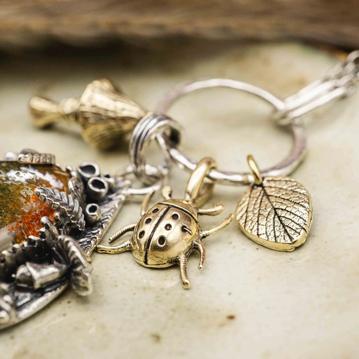 Statement Kette groß aus Silber 925. In den Anhänger eingefasst ist ein tropfenförmiger Lodolith, auch Gartenquarz genannt. Der Stein sieht aus wie eingeschlossenes grünes, gelbes und orangefarbenes Moos und ist umrandet von Pilzen, Blättern und Knospen. Ein echtes, handgefertigtes Statement Piece an Naturschmuck.
An dem Anhänger hängen außerdem 3 kleine Charms aus Messing: Ein Marienkäfer, ein Pilz und ein Blatt.