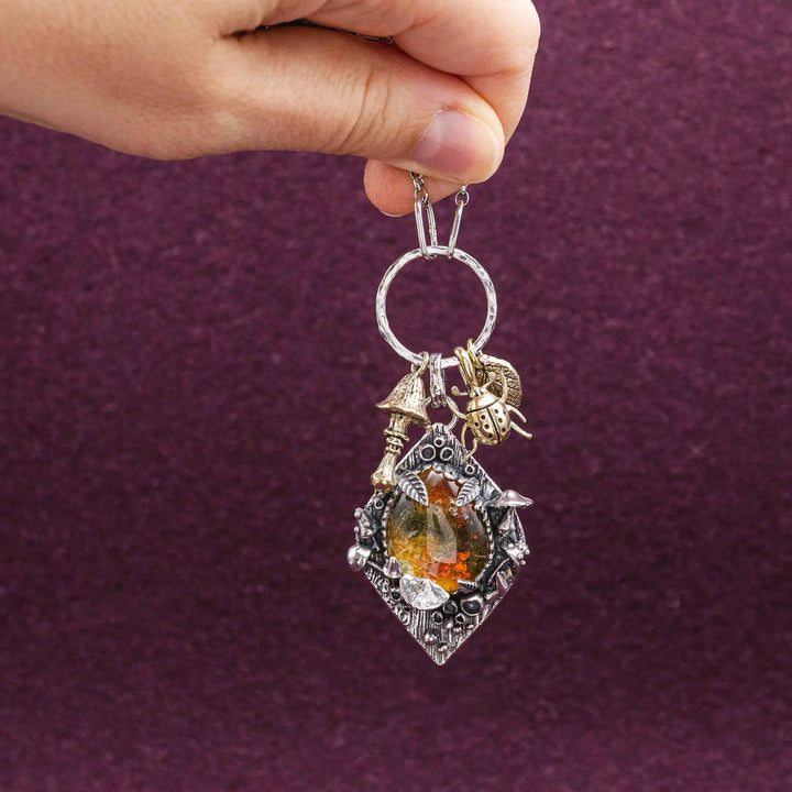 Statement Kette groß aus Silber 925. In den Anhänger eingefasst ist ein tropfenförmiger Lodolith, auch Gartenquarz genannt. Der Stein sieht aus wie eingeschlossenes grünes, gelbes und orangefarbenes Moos und ist umrandet von Pilzen, Blättern und Knospen. Ein echtes, handgefertigtes Statement Piece an Naturschmuck.
An dem Anhänger hängen außerdem 3 kleine Charms aus Messing: Ein Marienkäfer, ein Pilz und ein Blatt.