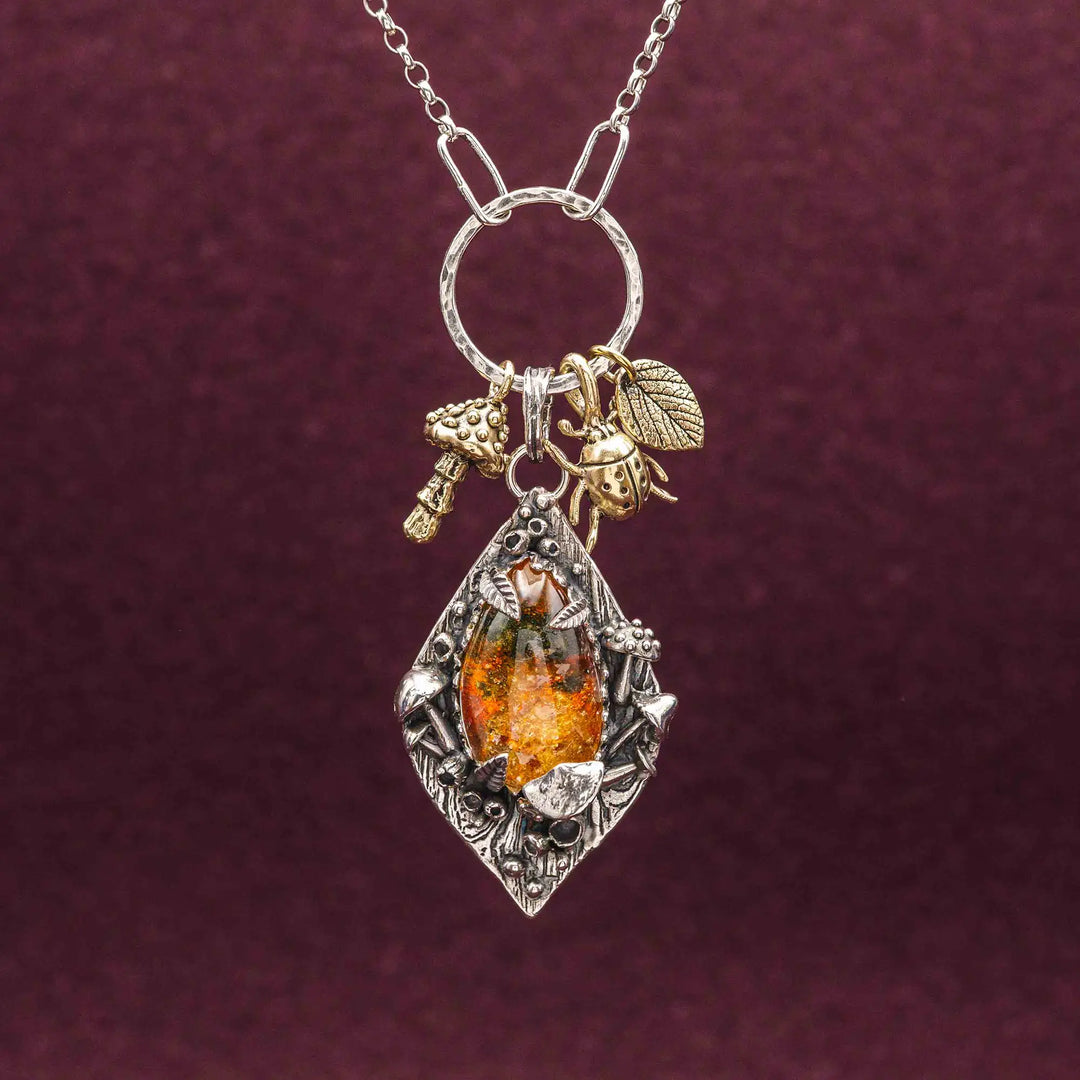 Statement Kette groß aus Silber 925. In den Anhänger eingefasst ist ein tropfenförmiger Lodolith, auch Gartenquarz genannt. Der Stein sieht aus wie eingeschlossenes grünes, gelbes und orangefarbenes Moos und ist umrandet von Pilzen, Blättern und Knospen. Ein echtes, handgefertigtes Statement Piece an Naturschmuck.
An dem Anhänger hängen außerdem 3 kleine Charms aus Messing: Ein Marienkäfer, ein Pilz und ein Blatt.