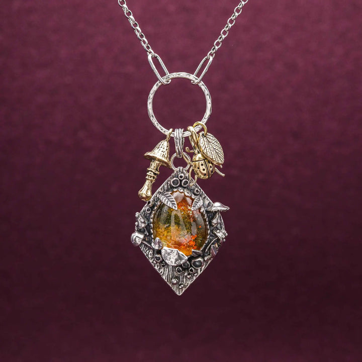 Statement Kette groß aus Silber 925. In den Anhänger eingefasst ist ein tropfenförmiger Lodolith, auch Gartenquarz genannt. Der Stein sieht aus wie eingeschlossenes grünes, gelbes und orangefarbenes Moos und ist umrandet von Pilzen, Blättern und Knospen. Ein echtes, handgefertigtes Statement Piece an Naturschmuck.
An dem Anhänger hängen außerdem 3 kleine Charms aus Messing: Ein Marienkäfer, ein Pilz und ein Blatt.