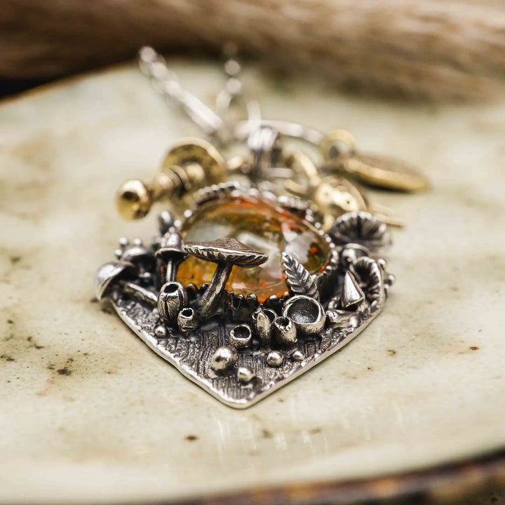 Statement Kette groß aus Silber 925. In den Anhänger eingefasst ist ein tropfenförmiger Lodolith, auch Gartenquarz genannt. Der Stein sieht aus wie eingeschlossenes grünes, gelbes und orangefarbenes Moos und ist umrandet von Pilzen, Blättern und Knospen. Ein echtes, handgefertigtes Statement Piece an Naturschmuck.
An dem Anhänger hängen außerdem 3 kleine Charms aus Messing: Ein Marienkäfer, ein Pilz und ein Blatt.