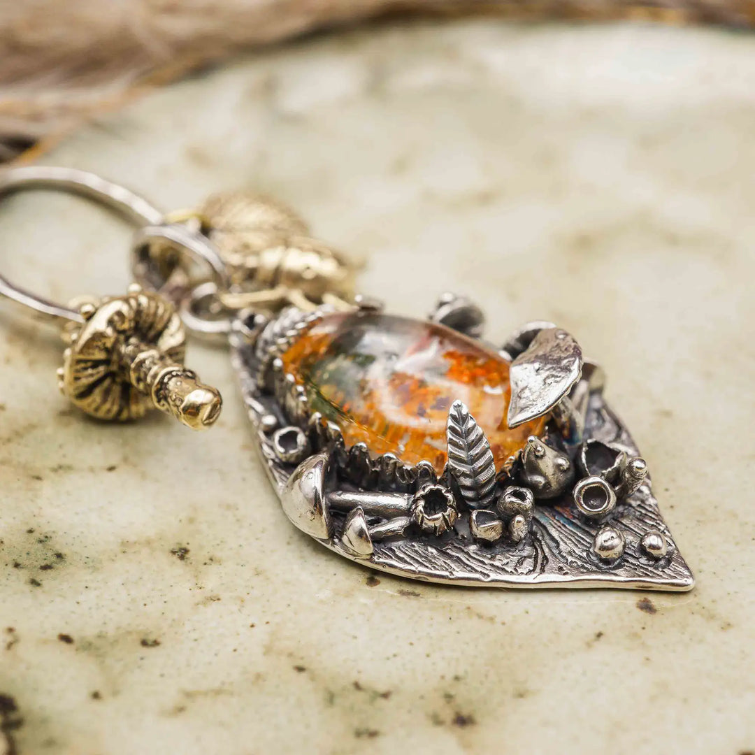 Statement Kette groß aus Silber 925. In den Anhänger eingefasst ist ein tropfenförmiger Lodolith, auch Gartenquarz genannt. Der Stein sieht aus wie eingeschlossenes grünes, gelbes und orangefarbenes Moos und ist umrandet von Pilzen, Blättern und Knospen. Ein echtes, handgefertigtes Statement Piece an Naturschmuck.
An dem Anhänger hängen außerdem 3 kleine Charms aus Messing: Ein Marienkäfer, ein Pilz und ein Blatt.
