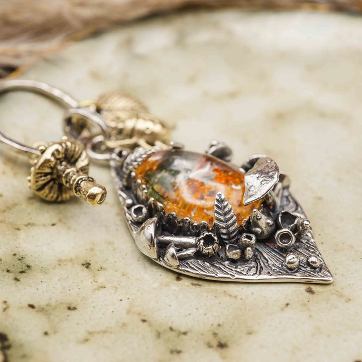 Statement Kette groß aus Silber 925. In den Anhänger eingefasst ist ein tropfenförmiger Lodolith, auch Gartenquarz genannt. Der Stein sieht aus wie eingeschlossenes grünes, gelbes und orangefarbenes Moos und ist umrandet von Pilzen, Blättern und Knospen. Ein echtes, handgefertigtes Statement Piece an Naturschmuck.
An dem Anhänger hängen außerdem 3 kleine Charms aus Messing: Ein Marienkäfer, ein Pilz und ein Blatt.